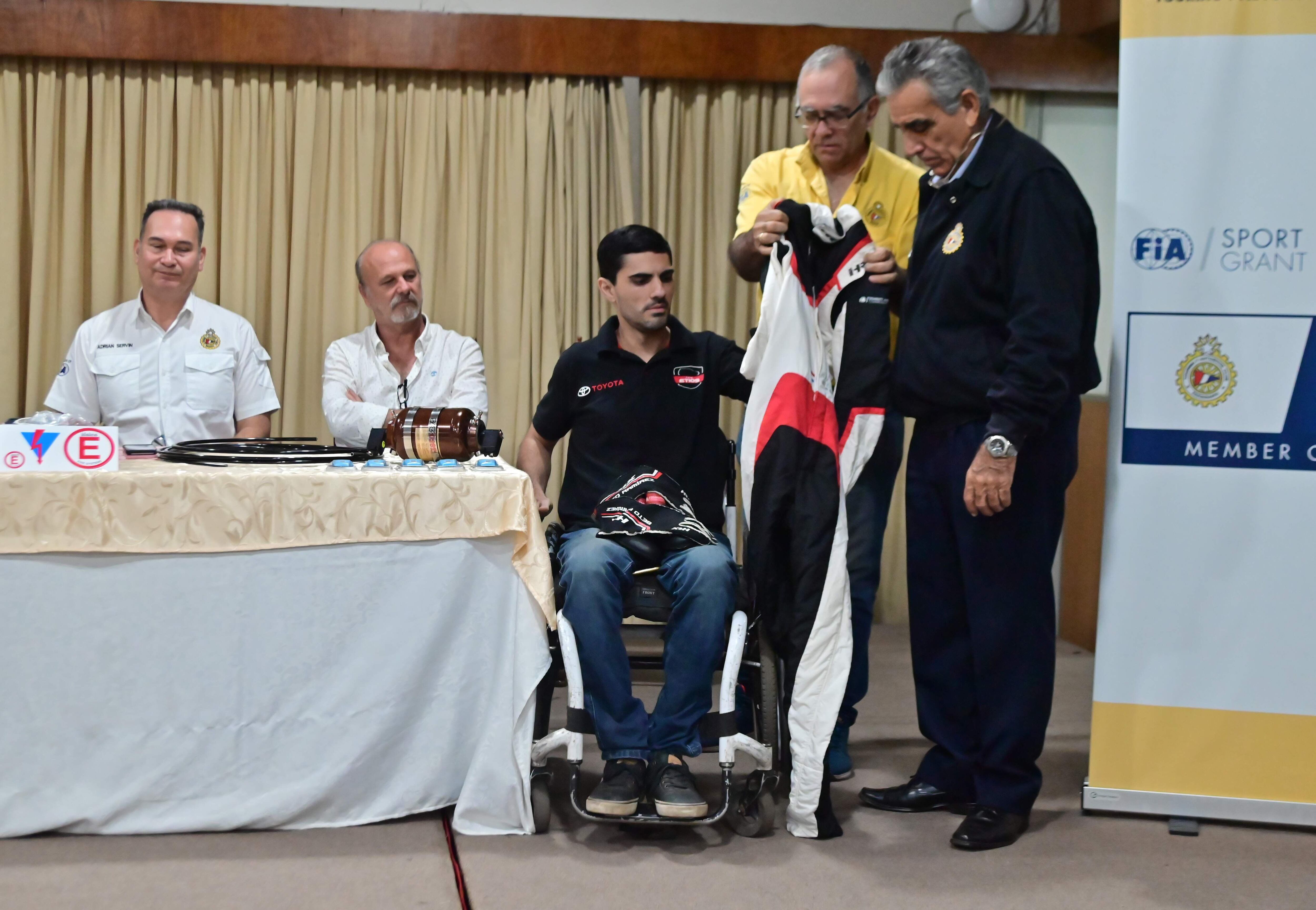 Edgar Molas y Ramón Galeano hacen entrega de un buzo antiflamas donado por la FIA a Federico “Beto” Ramírez.