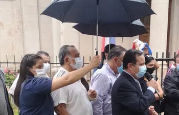 Una mujer sostiene un paraguas para los senadores Richer y Pereira y para el diputado Vera Bejarano.