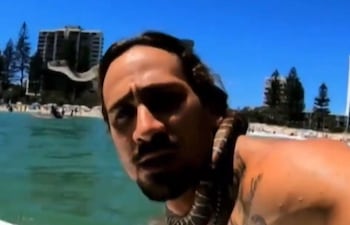 El surfista Higor Fiuza en una captura de pantalla sufeando con una serpiente pitón enroscada al cuello. El deportista recibió una multa de USD 1.500.