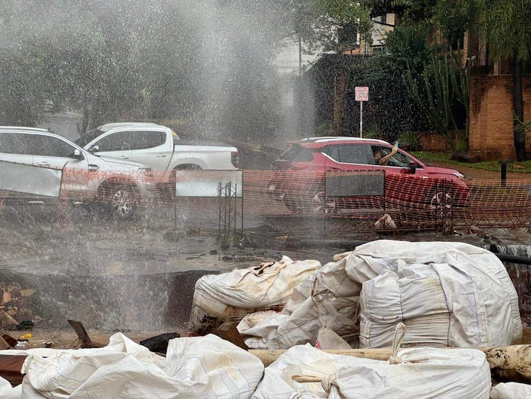 Automóvil rojo con pasajero grabando, sacos de construcción y barrera de seguridad en un ambiente húmedo y caótico.
