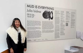 Julia Isídrez, con chaqueta negra y chal blanco, junto a un panel informativo en la exposición 'MUD IS EVERYTHING'.