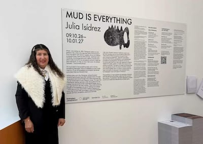 Julia Isídrez, con chaqueta negra y chal blanco, junto a un panel informativo en la exposición 'MUD IS EVERYTHING'.