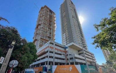 Edificios en construcción de diseño moderno y tradicional, con andamiaje y valla publicitaria visible en un entorno urbano.