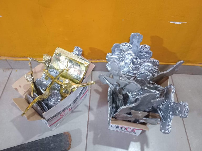 Cajas de cartón con objetos metálicos dorados y plateados en un entorno con pared naranja.