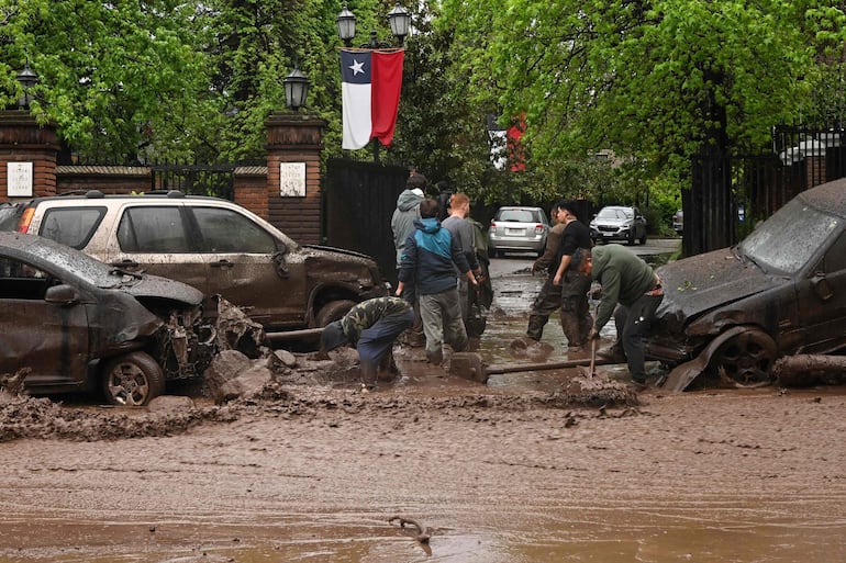 Residents remove mud and debris from vehicles damaged by a mudslide in the Las Condes district of Santiago on October 8, 2026. (Photo by RODRIGO ARANGUA / AFP)
