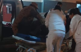 Mujer indígena en camilla rodeada de tres profesionales de salud con uniformes blancos en una escena de emergencia.