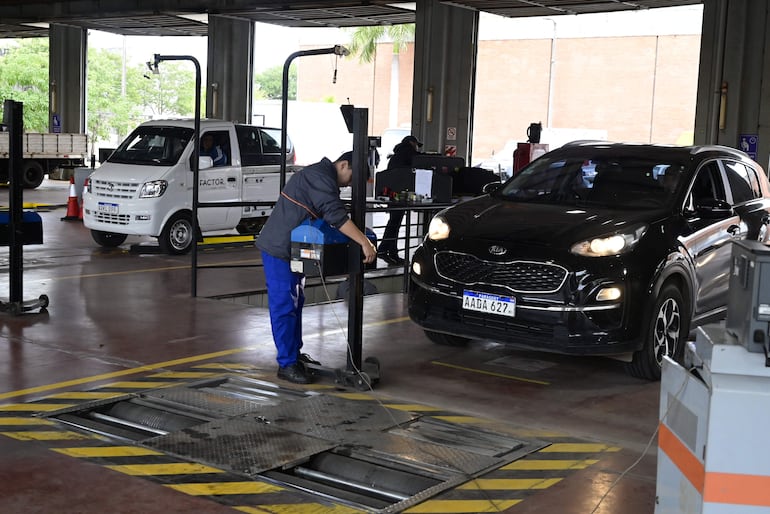 Operario en ropa de trabajo revisa coche negro Kia con dispositivo en un taller iluminado.
