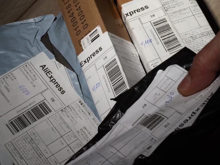 Paquetes de AliExpress dispuestos en una superficie, con un dedo sosteniendo uno de ellos en un entorno de oficina.
