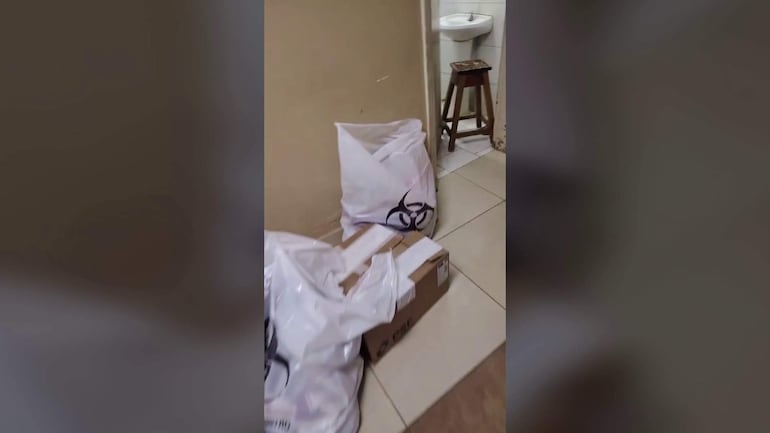 Pasillo con dos bolsas peligrosas en el suelo y un lavamanos. Ambiente descuidado y desordenado.