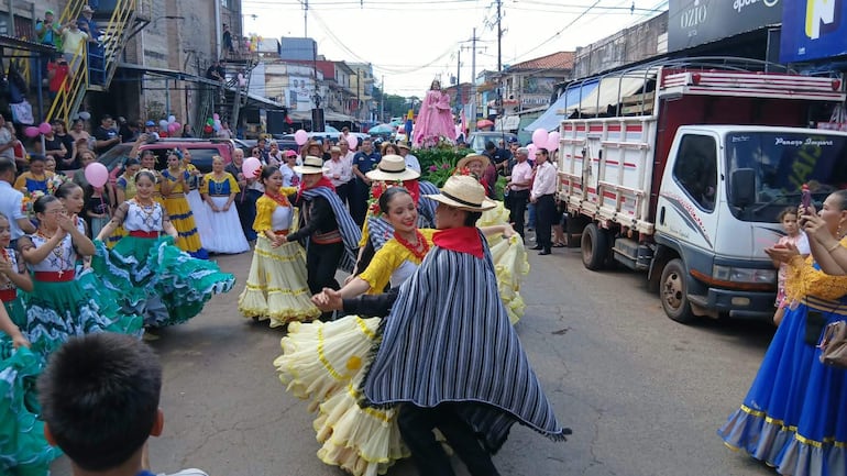 Cuatro bailarines en trajes coloridos realizan danza tradicional con un público entusiasta y decoraciones festivas.