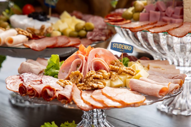Platter de charcutería con jamón, salami, quesos, nueces y lechuga, en una mesa elegante sin personas presentes.