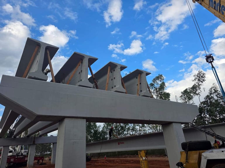 Estructura de hormigón elevada sujeta por grúas en un entorno de construcción con cielo parcialmente nublado.