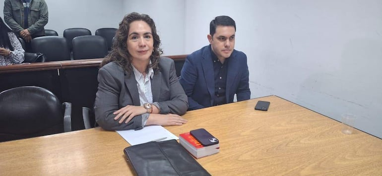 Alba Záracho con blazer gris y blusa blanca junto a Hernán Rivas con camisa negra y blazer azul, en una mesa con documentos.
