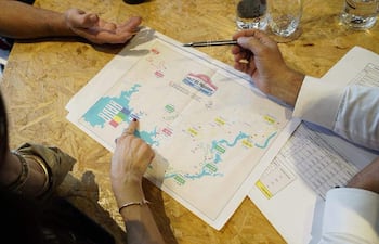 Manos sobre un mapa y documentos en mesa de trabajo, indicando planificación para el Rally del Paraguay.