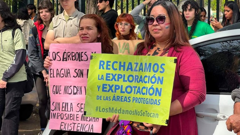 Seis personas en una protesta, sosteniendo carteles sobre la protección ambiental, con expresiones de preocupación en un ambiente urbano.
