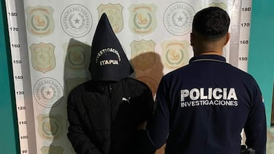 Hombre encapuchado y policía de espaldas en un entorno interior con insignias policiales visibles.