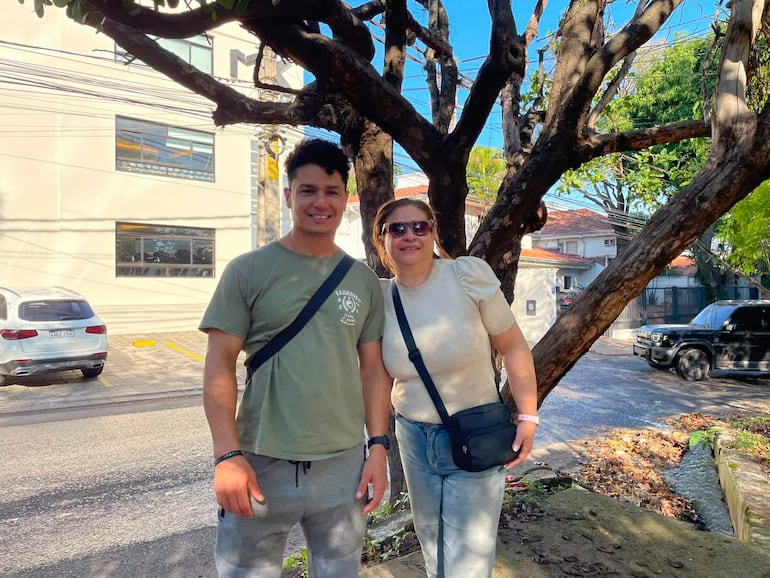 Hombre joven con camiseta verde y pantalones claros sonríe junto a mujer de blusa beige y jeans.