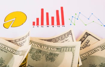 Imagen alusiva a finanzas. Se ven billetes de dólares sobre un fondo de gráficos.