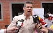 Santiago Peña de pie, sosteniendo un micrófono, rodeado de periodistas, con pared del Ministerio de Urbanismo al fondo.