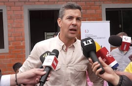 Santiago Peña de pie, sosteniendo un micrófono, rodeado de periodistas, con pared del Ministerio de Urbanismo al fondo.