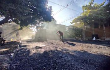 Dos obreros en Asunción, uno con pala y otro operando un rodillo en un día soleado, rodeados de vegetación y casas urbanas.
