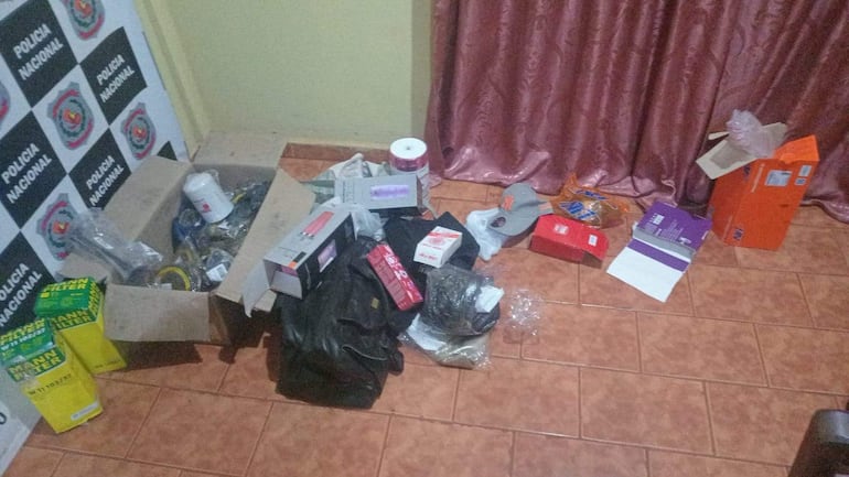 Oficina desordenada con cajas y productos variados, sin personas presentes, enmarcada por un emblema de la Policía Nacional.