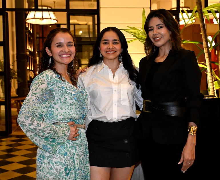 Tres mujeres sonrientes en el Hotel Palmaroga; una con vestido de flores, otra con camisa blanca y la última en atuendo negro con accesorios dorados.