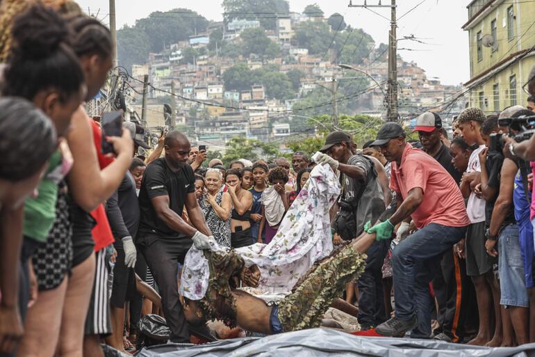CONTENIDO GRÁFICO EXPLICITO. Personas acomodan cuerpos sin vida en una calle este miércoles, en Río de Janeiro (Brasil). La operación policial lanzada el martes en Río de Janeiro, la más letal de la historia de la ciudad brasileña, dejó 132 muertos, entre ellos cuatro agentes.