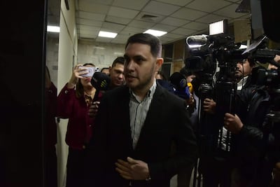 Hernán Rivas, con traje oscuro y expresión tranquila, habla rodeado de periodistas con micrófonos y cámaras en un ambiente iluminado.