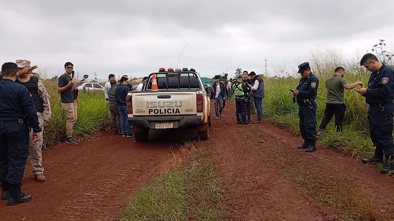 Policías en uniforme revisan sus teléfonos cerca de una camioneta Isuzu, mientras un hombre sostiene un micrófono en el centro.