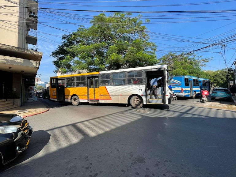 Autobús blanco y amarillo número 97 gira en intersección urbana, rodeado de vehículos y edificios.