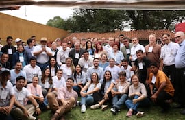 Miembros del partido Patria Querida sonríen y conversan en un ambiente al aire libre, con identificaciones visibles. Fondo amarillo y techado con tejas.