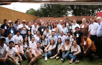 Miembros del partido Patria Querida sonríen y conversan en un ambiente al aire libre, con identificaciones visibles. Fondo amarillo y techado con tejas.
