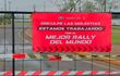 Cartel de advertencia en la vía pública con texto sobre el Rally de Paraguay, entorno urbano y áreas verdes visibles.
