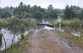 Vista de un camino de tierra y área inundada con dos pequeñas embarcaciones ancladas en un cielo nublado.