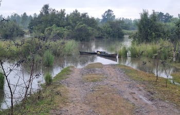 Vista de un camino de tierra y área inundada con dos pequeñas embarcaciones ancladas en un cielo nublado.