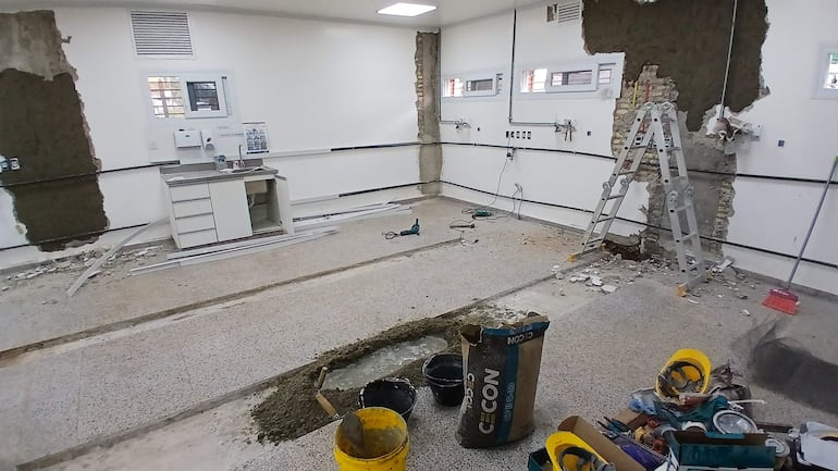 Ambiente en remodelación con paredes blancas, escalera de aluminio y escombros en el suelo.