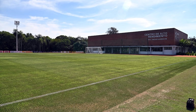 Campo de entrenamiento en césped con edificio moderno al fondo y árboles en la periferia.