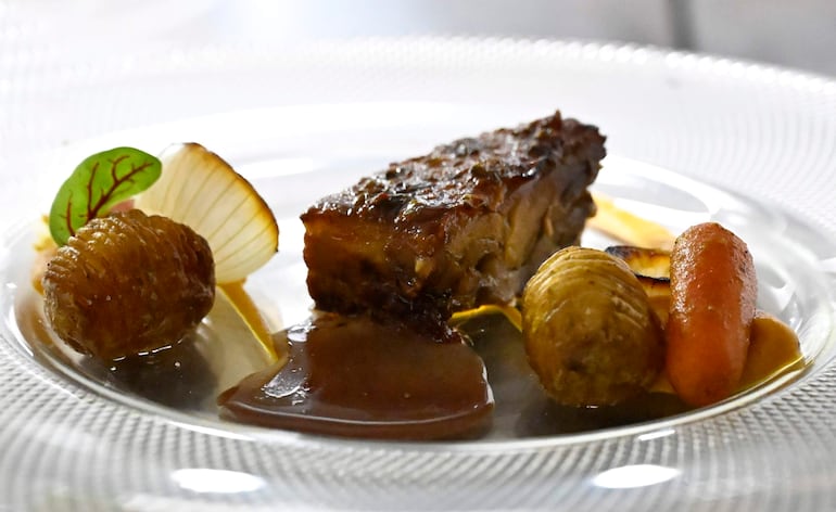 Plato gourmet con carne asada, zanahoria asada y guarniciones vegetales en ambiente de alta cocina.