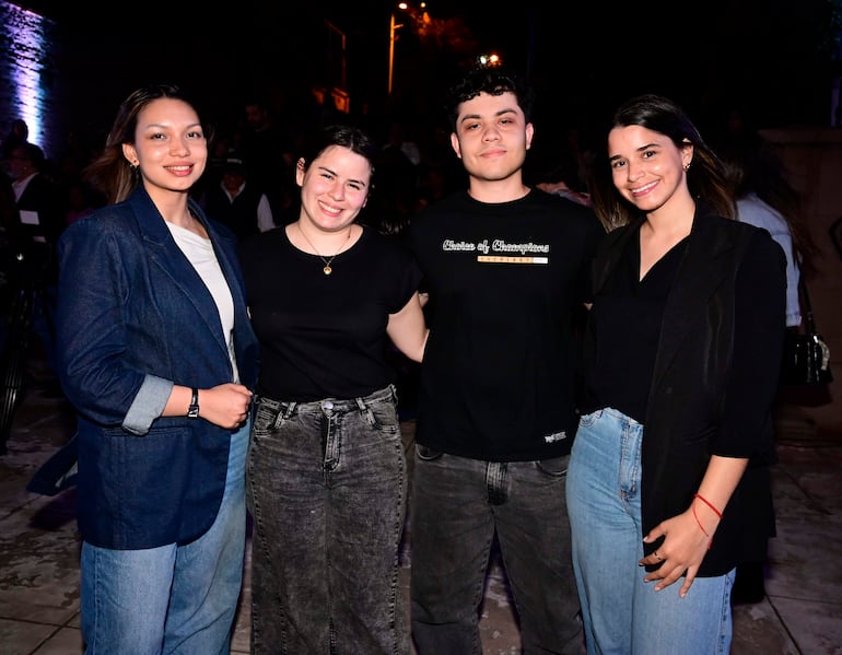 Mujeres sonrientes con blazers y camisetas, hombres con camiseta oscura, en ambiente nocturno de evento social.