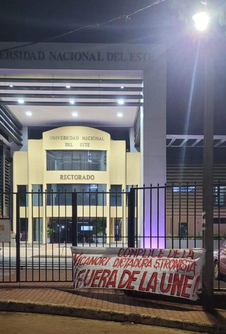 Edificio del Rectorado de la Universidad Nacional del Este, con pancarta de protesta iluminada en la noche.