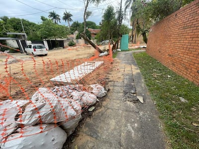 Cerca de seguridad naranja delimita el área de trabajo, con sacos de cemento y bloques de pavimento en un entorno urbano en construcción.
