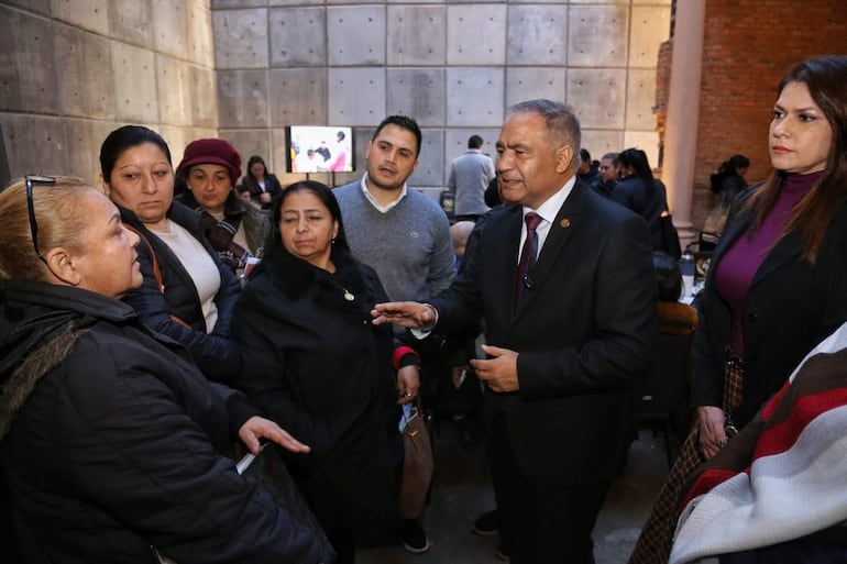 Javier Esquivel de chaqueta oscura gesticula mientras cinco mujeres lo observan atentamente en un ambiente elegante.