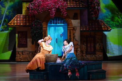 Mujeres en el escenario: una con vestido amarillo y otra con vestuario vibrante, en diálogo ameno entre decoraciones teatrales.