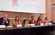Kattya González expone en conferencia, acompañada de Hugo González y otras panelistas en un ambiente de mesa con documentos.