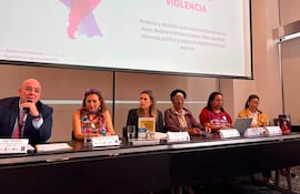 Kattya González expone en conferencia, acompañada de Hugo González y otras panelistas en un ambiente de mesa con documentos.