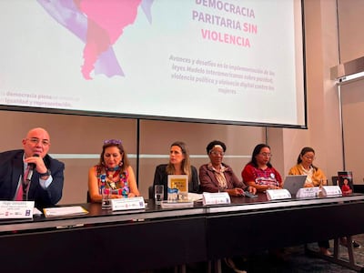 Kattya González expone en conferencia, acompañada de Hugo González y otras panelistas en un ambiente de mesa con documentos.