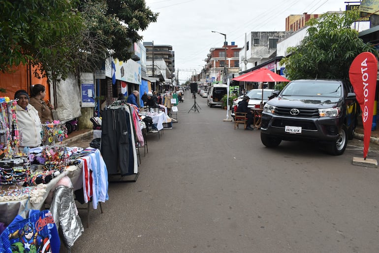 Mujer de chaqueta blanca y gorra conversa con vendedor en colorido mercadillo al aire libre en Encarnación.