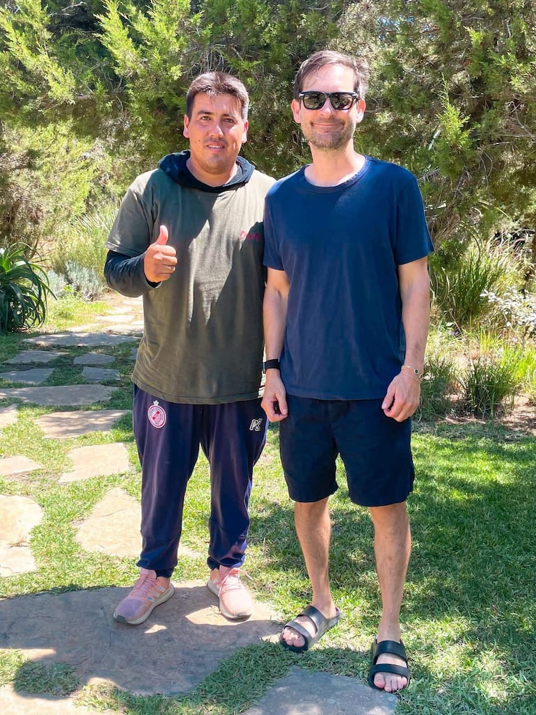 Richard Alfredo Aguilar Delgado y Tobey Maguire sonríen en un jardín, ambos con ropa informal, rodeados de vegetación.