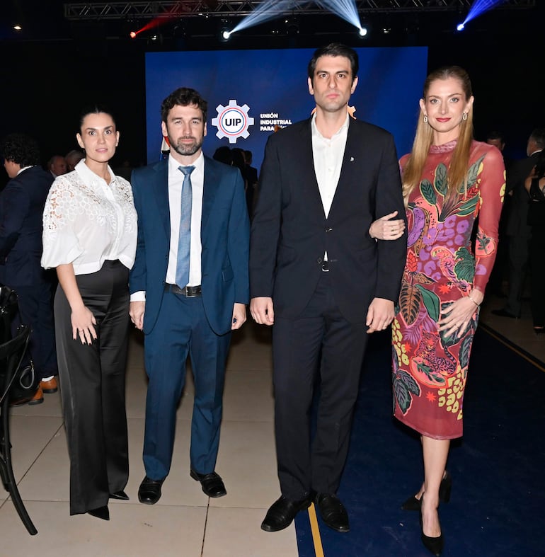 Guillermo Martinez en traje oscuro junto a dos hombres y una mujer, en un ambiente festivo con luces tenues y decoración formal.